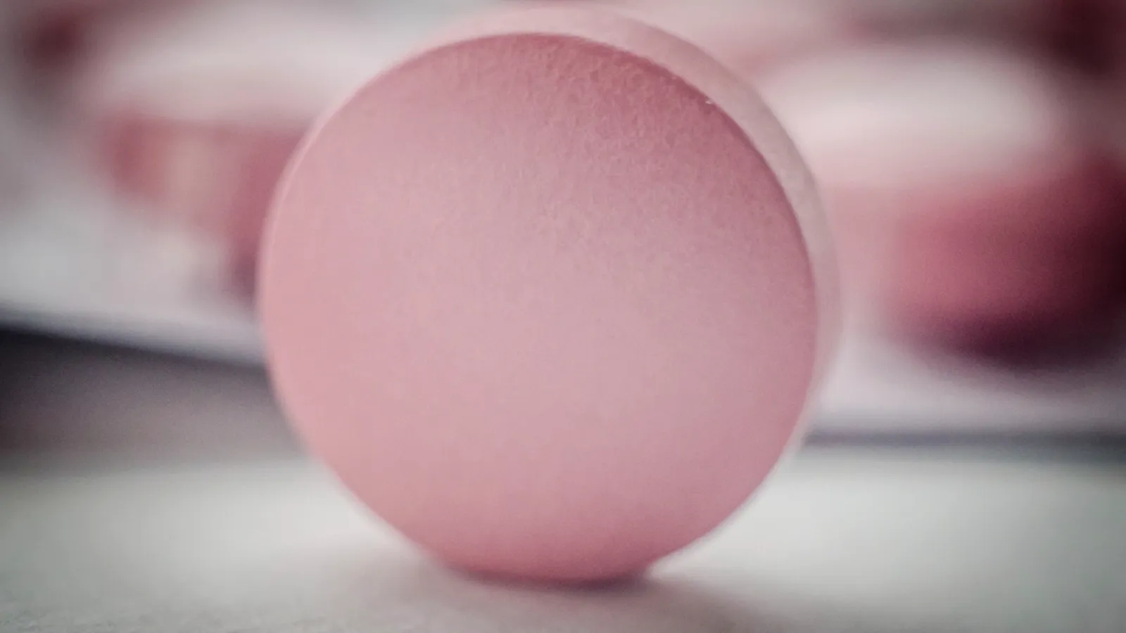 A single pink tablet in soft focus on a pale surface, representing hormone replacement therapy