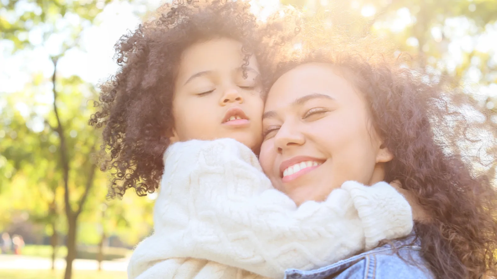 A smiling mother holding her young child close in warm sunlight, representing support for postpartum anxiety