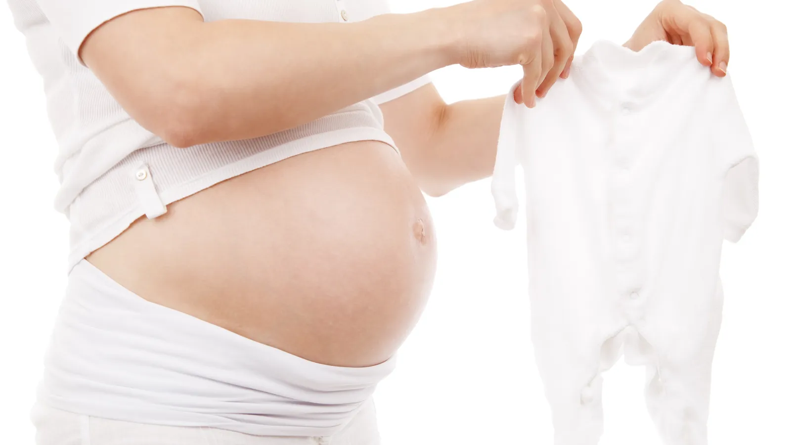 A pregnant woman in white holding up a small white babygrow beside her bump